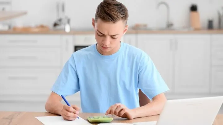 teen boy using calculator budgeting, looking puzzled