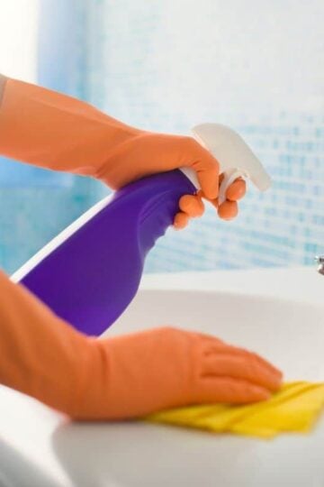 hands with orange gloves, using spray bottle to clean bathroom sink