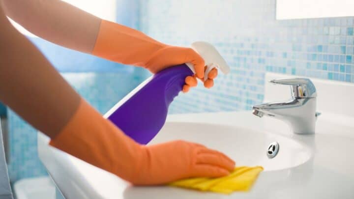 hands with orange gloves, using spray bottle to clean bathroom sink