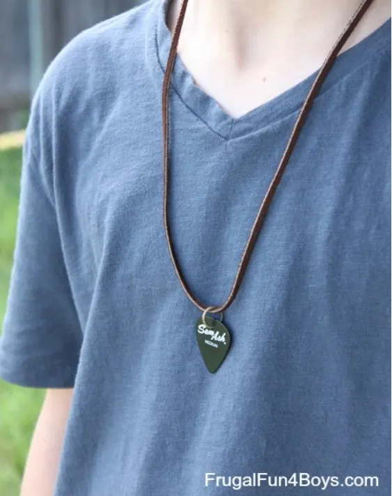 boy in blue shirt with necklace halfway down chest and guitar pick on it