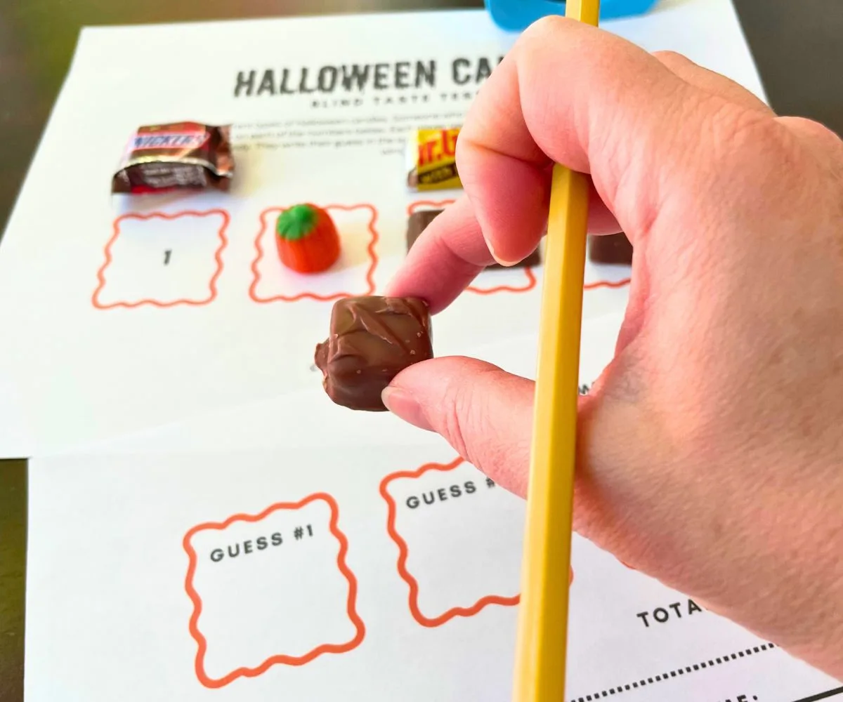 Hand holding pencil, and piece of candy, about to taste and fill out the guess chart