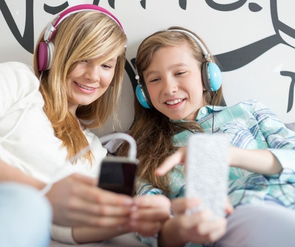 two teen girls listening to podcasts at slumber party, laughing