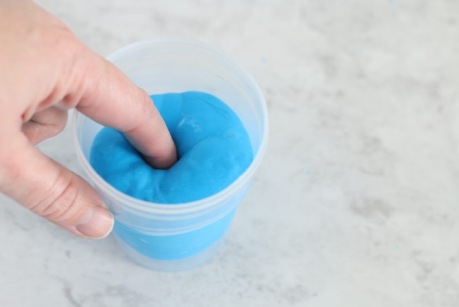 boy sticking finger into blue dough in a cup