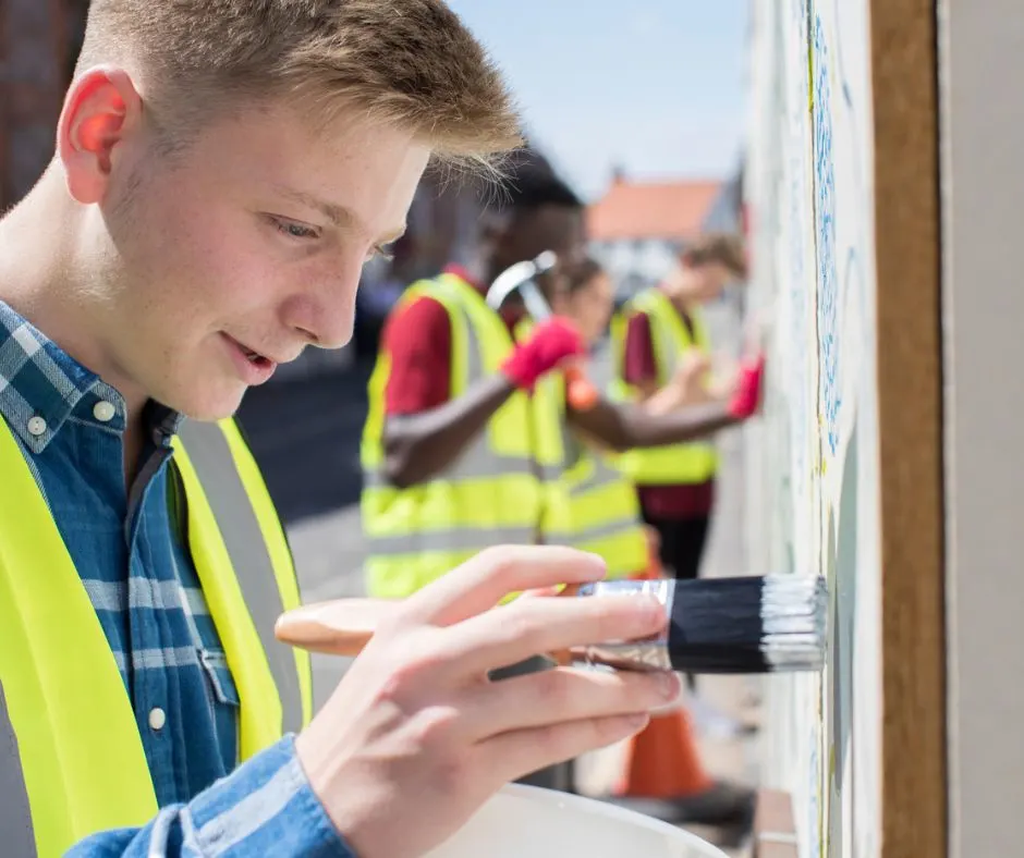 high school boy student painting mural on wall with other students