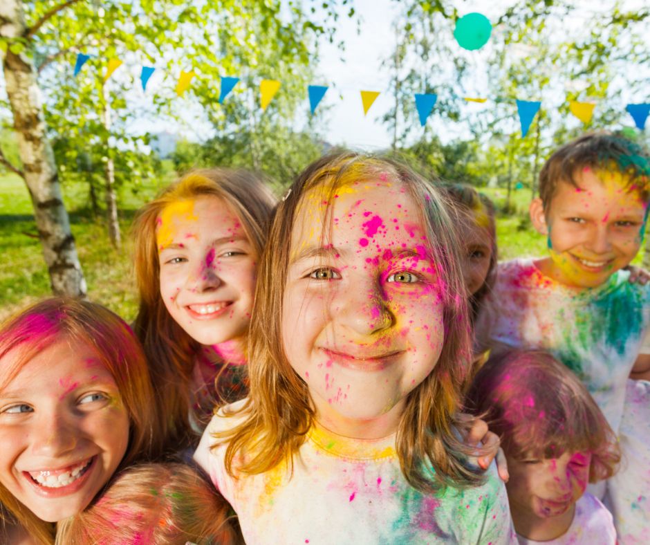 group of kids with holi colored powdered all over them, smiling in backyard