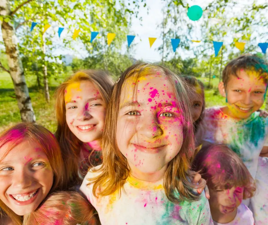 group of kids with holi colored powdered all over them, smiling in backyard