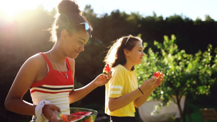 two tween girls in backyard with watermelon, smiling