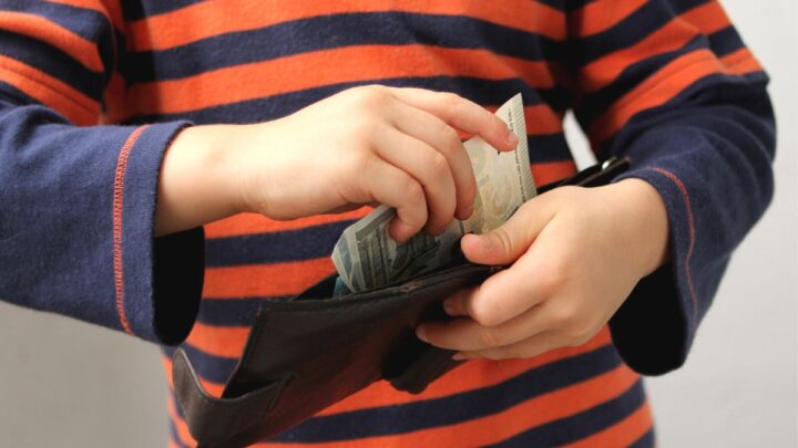 boy in orange striped shirt putting money into one of best wallet for children