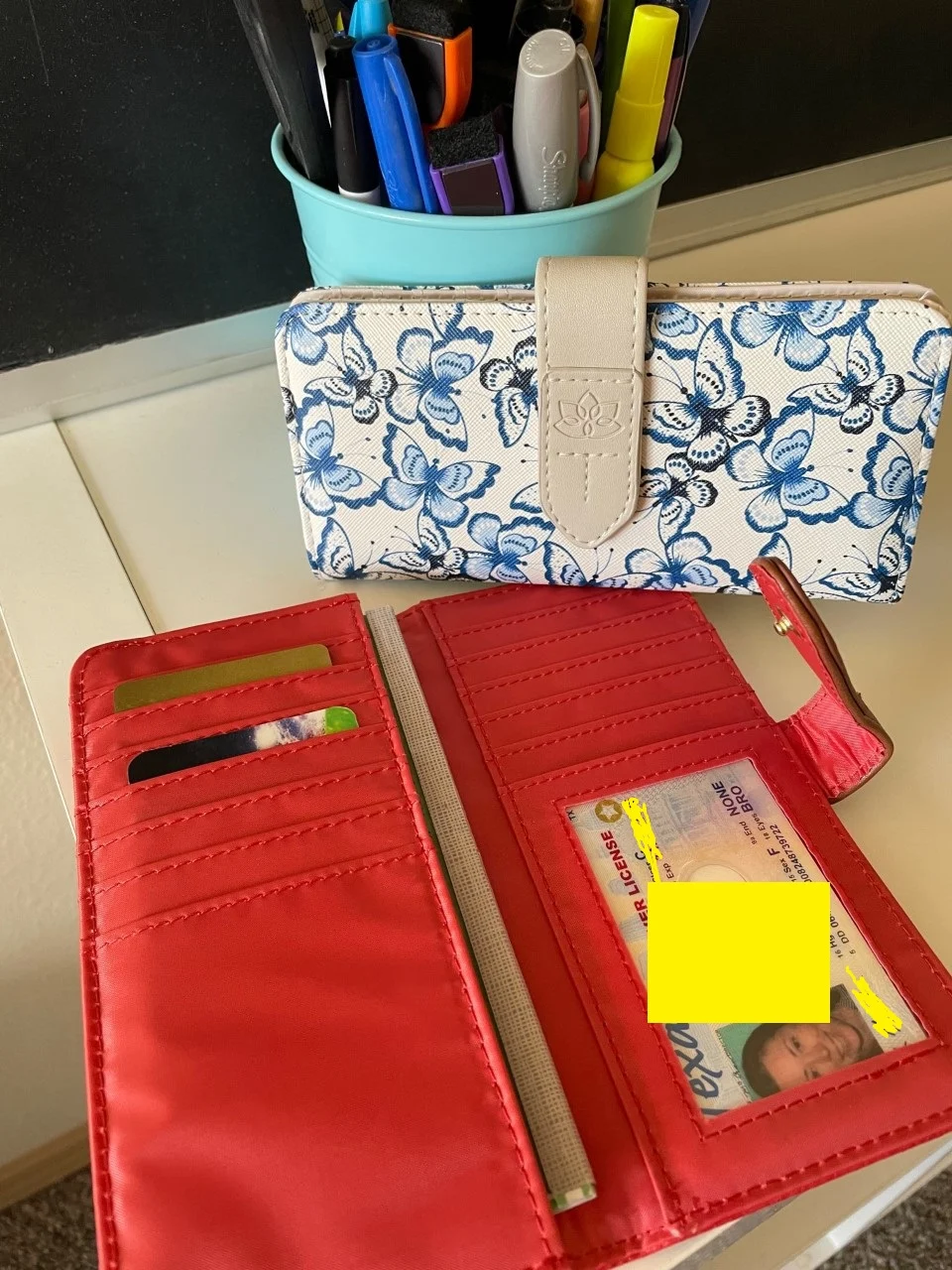 Alexandra Slim coral colored and blue and white butterfly colored wallets, with author's driver's license (sensitive info blurred out)