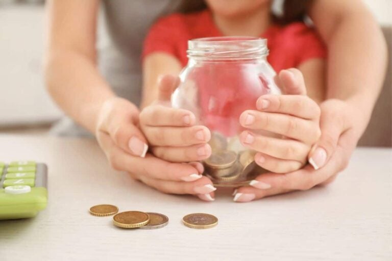 woman holding child's hand, who is holding a piggy bank with money