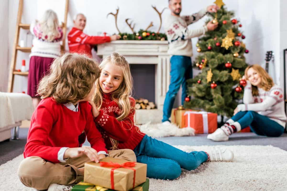 two kids doing Christmas activities with family in background, smiling