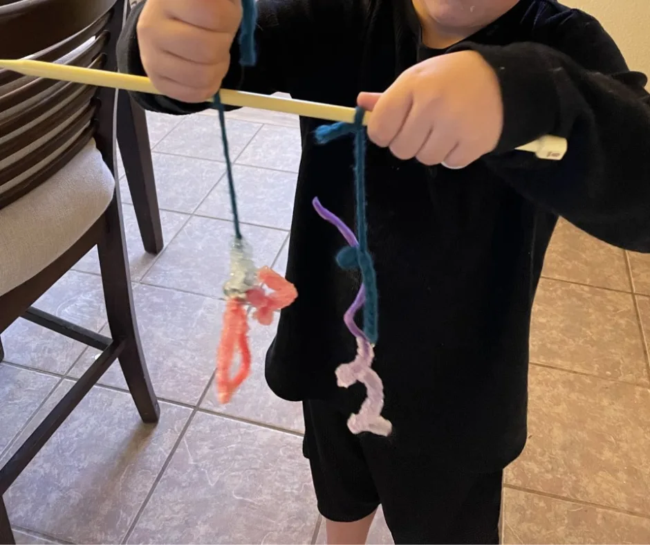 boy in black shirt holding up knitting needle with two completed borax crystal ornaments hanging down