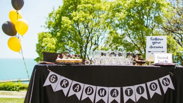 table at graduation party with graduation banner, yellow and black balloons, and treats