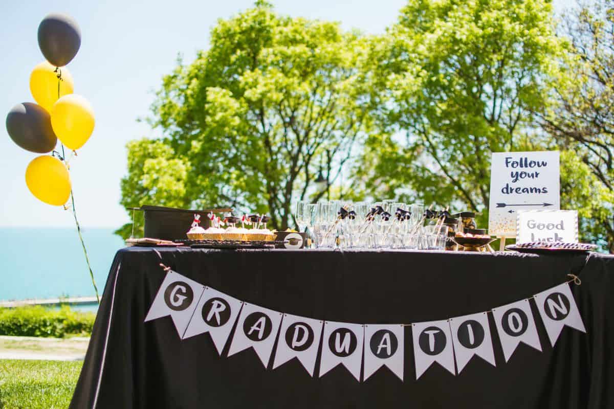 table at graduation party with graduation banner, yellow and black balloons, and treats