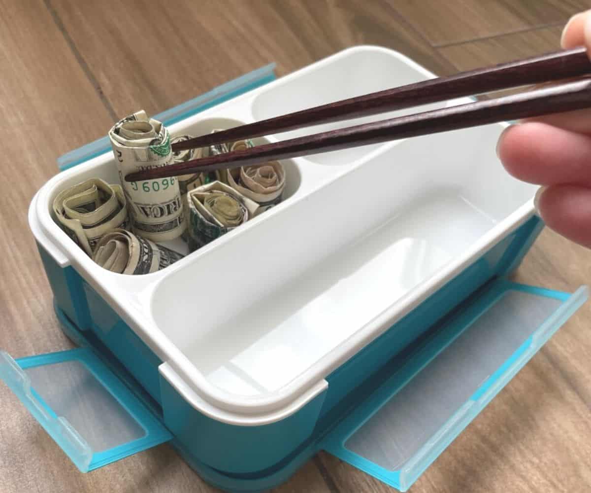 chopsticks picking up money sushi rolls in blue and white bento box