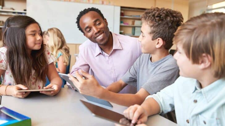 middle school teacher with students at table, smiling and working on consumer math project