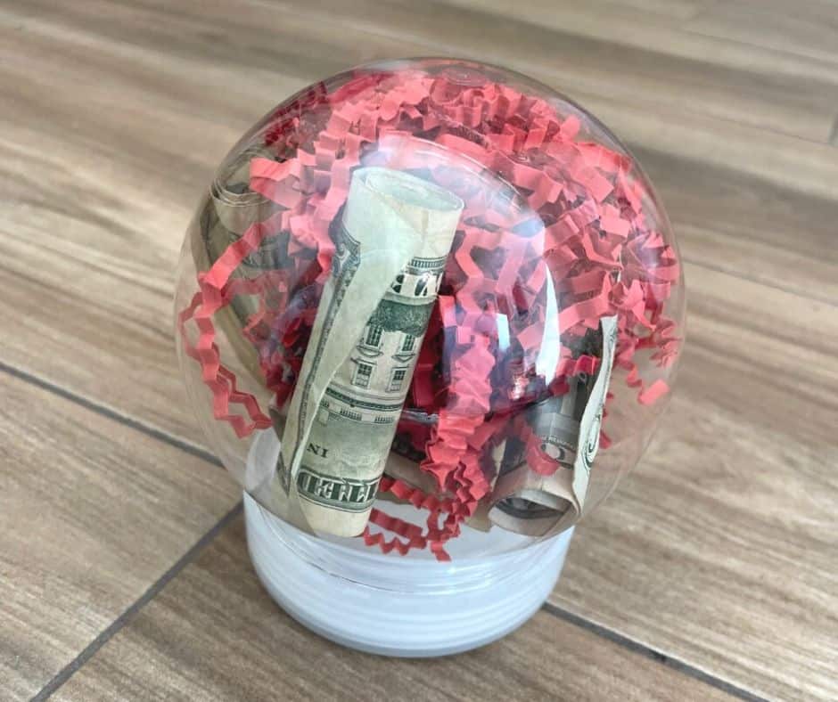 plastic snow globe filled with rolled up money and red confetti