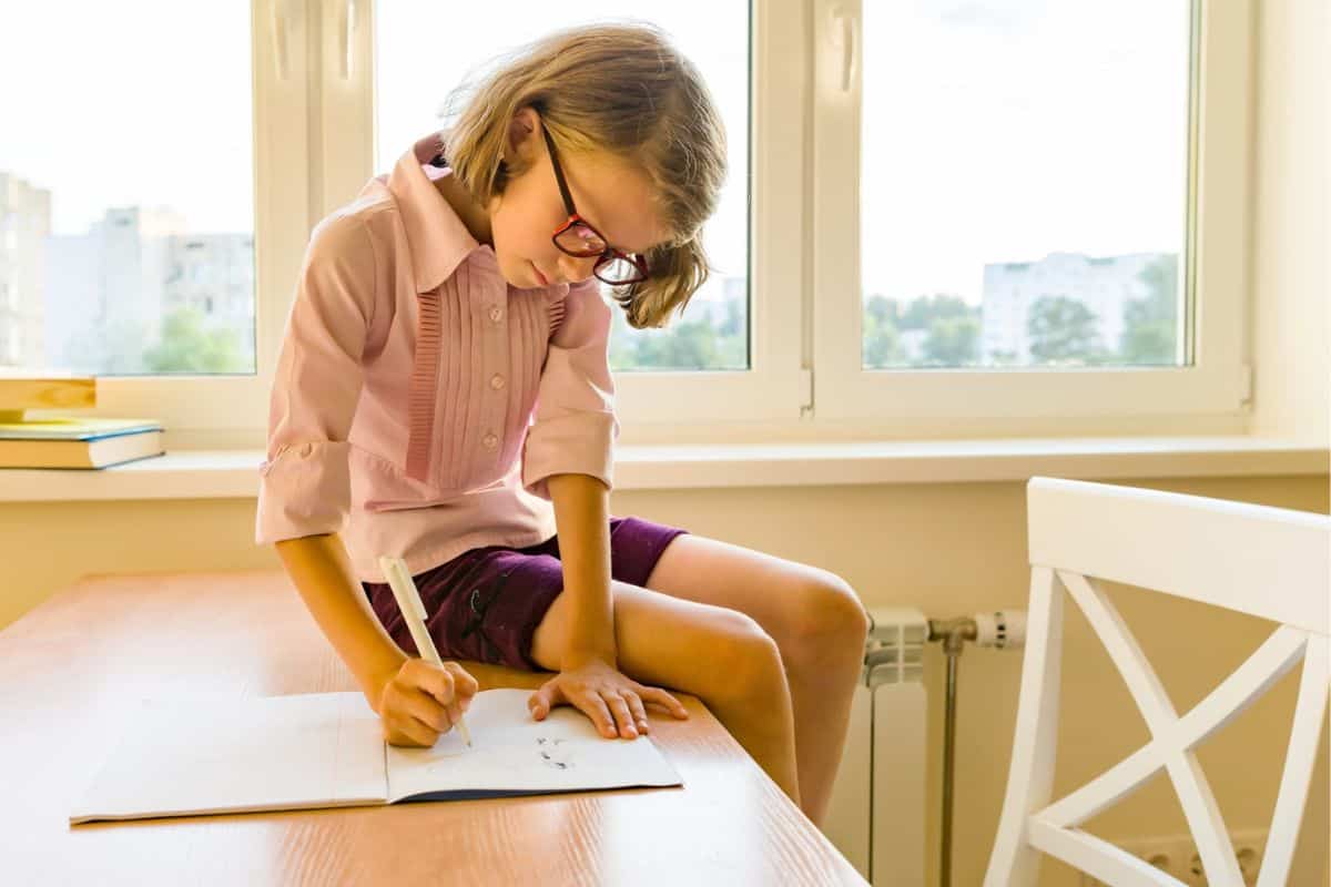 girl child sitting on desk filling in her printable savings challenge