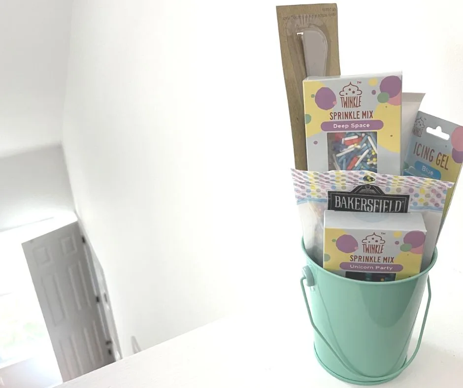 teal tin filled with different sprinkles, gels, and cake decorating tools