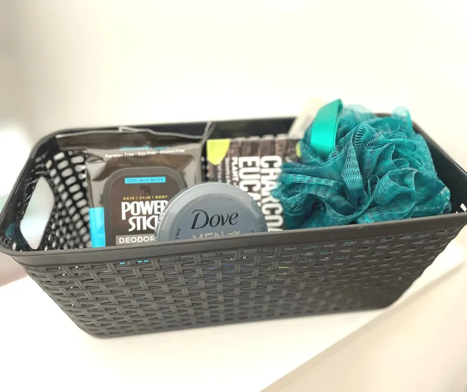 black storage container with several black dude skincare and bath products plus a green pouf