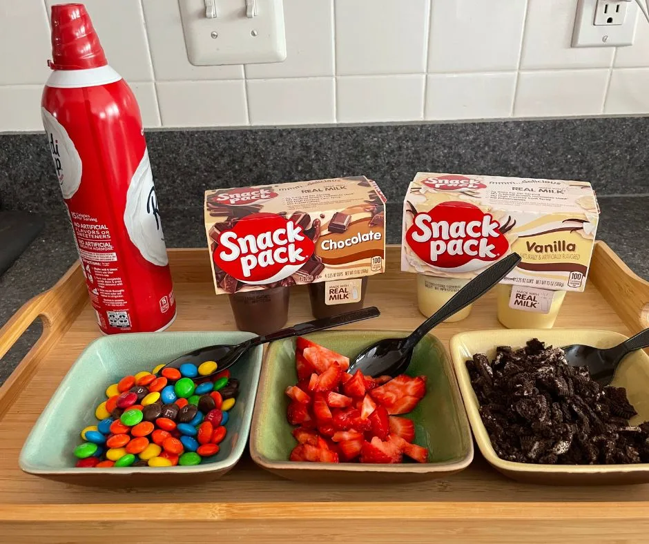 chocolate and vanilla puddings with whipped cream, strawberries, chopped cookies and M&Ms on wooden tray