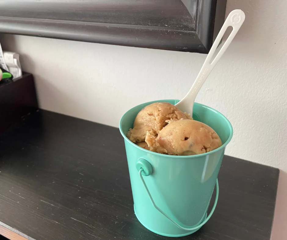 light teal tin of ice-cream scooped raw cookie dough on black table