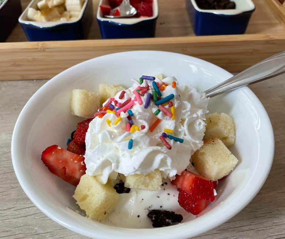white bowl with vanilla yogurt, strawberries, crushed cookies, whipped cream and sprinkles