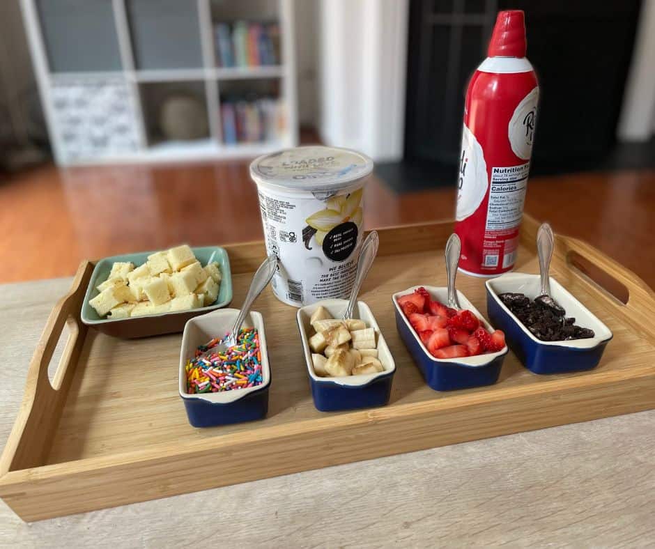 wooden tray filled with vanilla bean protein yogurt, chopped bananas, strawberries, pound cake, sprinkles, etc. 