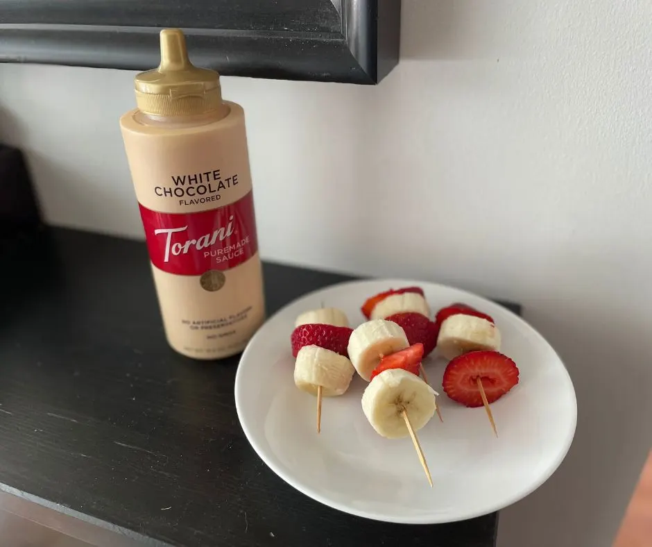 fruit kebabs on white plate with white chocolate sauce drizzled