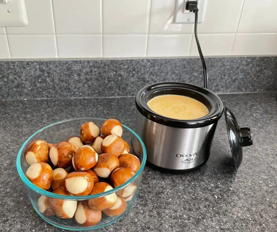 mini crockpot with cheese sauce inside, and glass bowl of pretzel bites on counter