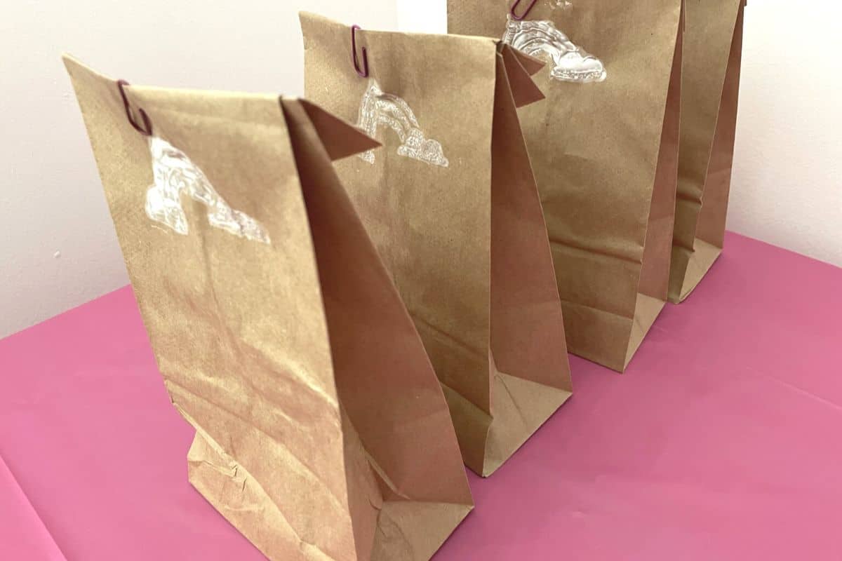 four lunch bags with stenciled white rainbow on it, on pink tablecloth