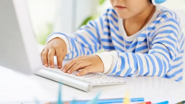 elementary student in blue striped shirt at desk playing online money game