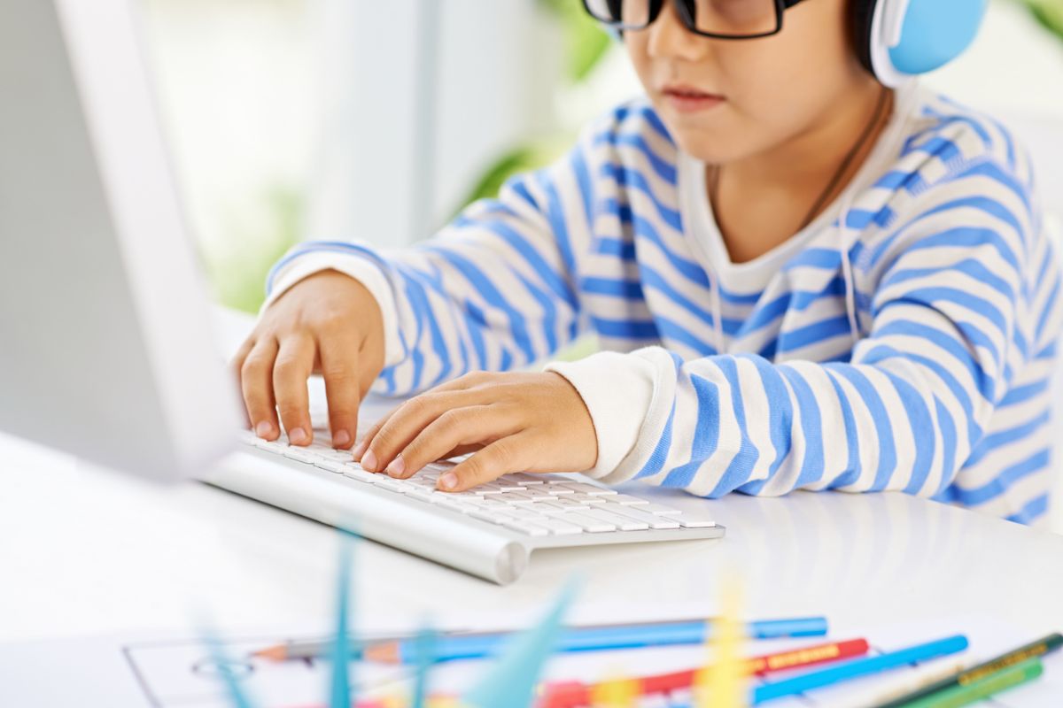 elementary student in blue striped shirt at desk playing online money game