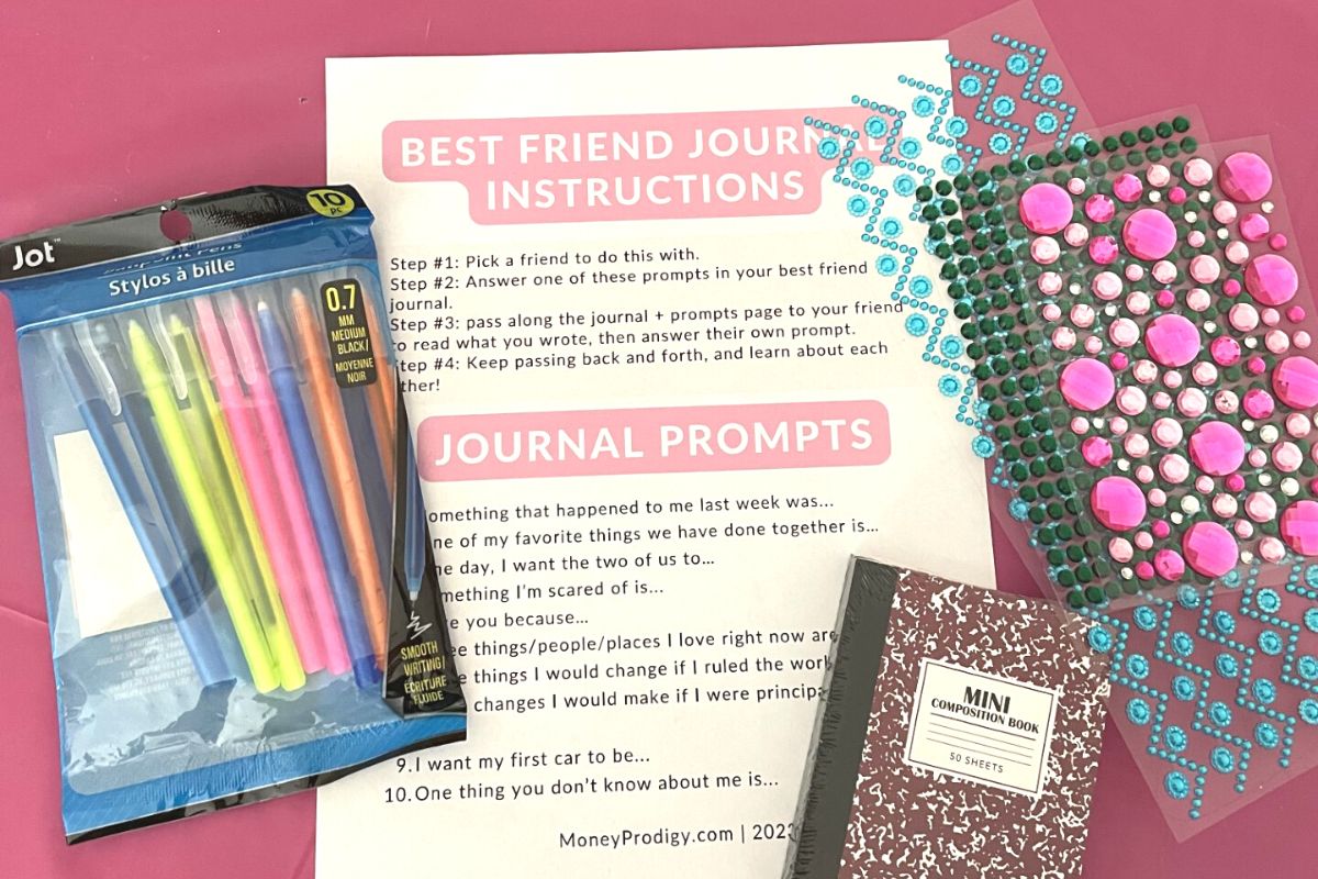 pens, gem stickers, mini journals, and journal prompt page on pink tablecloth