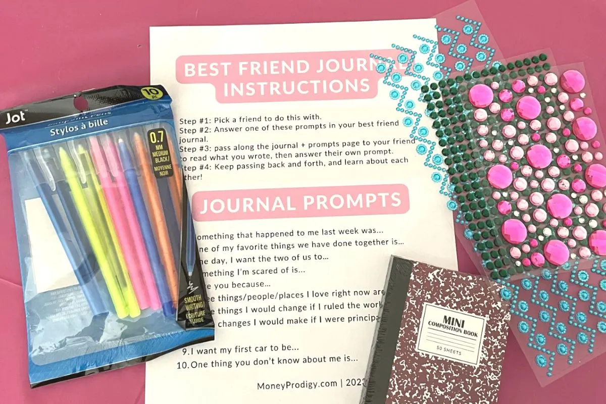 pens, gem stickers, mini journals, and journal prompt page on pink tablecloth
