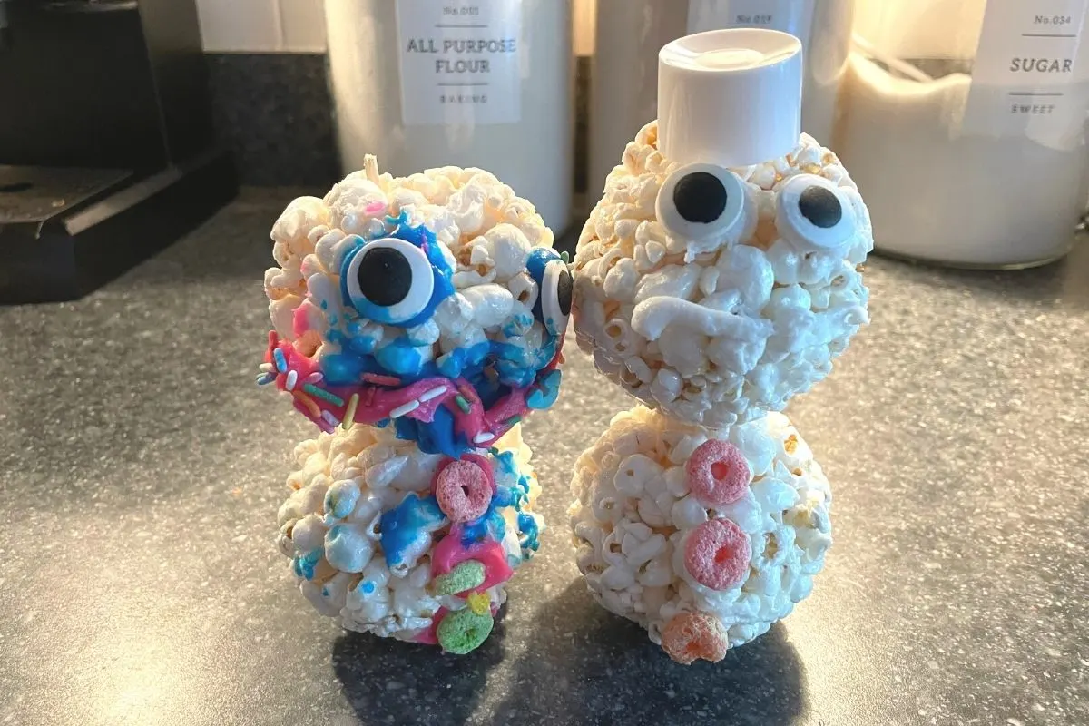 two decorated popcorn snowmen with candy eyeballs, fruit loop buttons, and icing