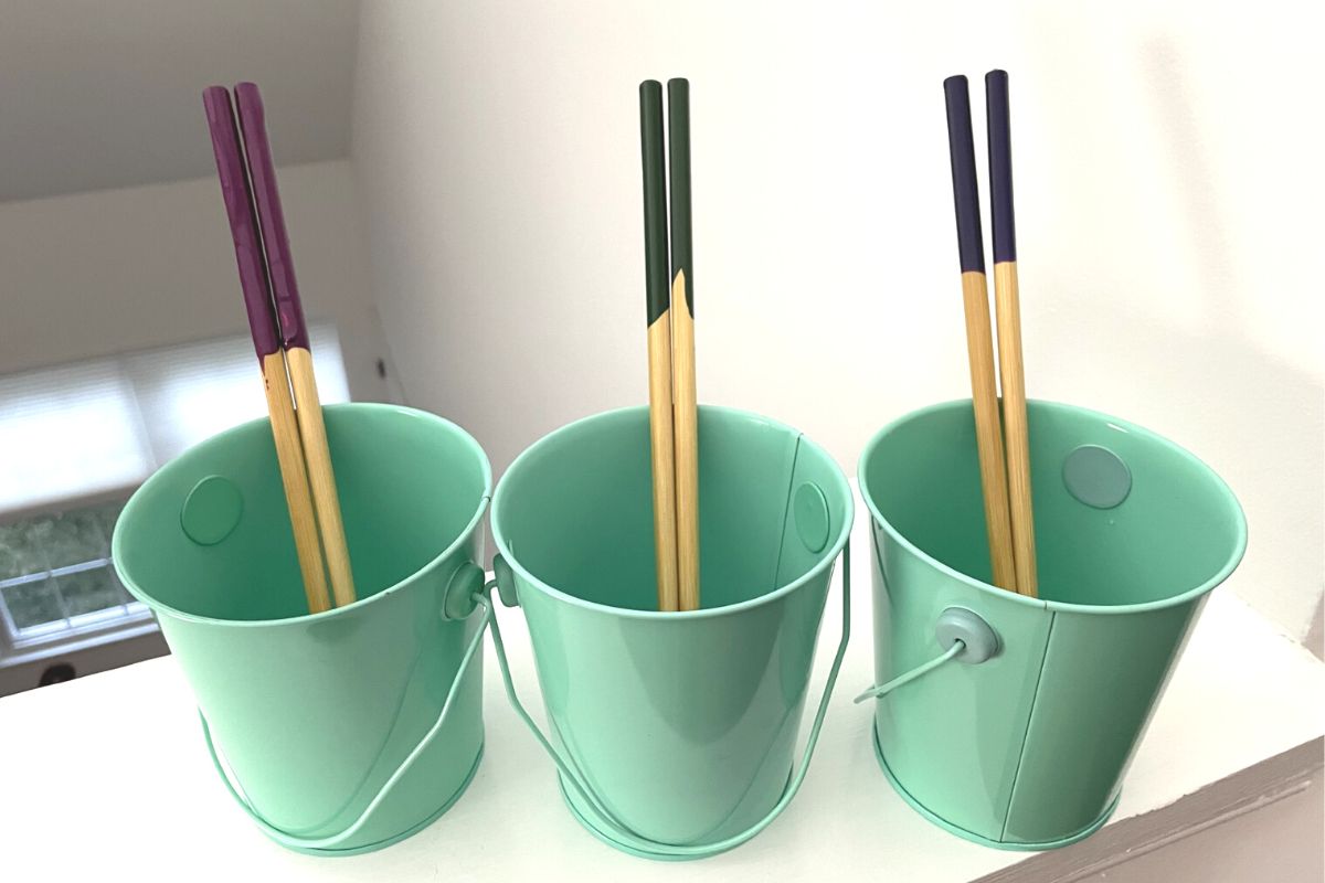 three teal colored buckets with one different colored chopsticks dipped in paint in each