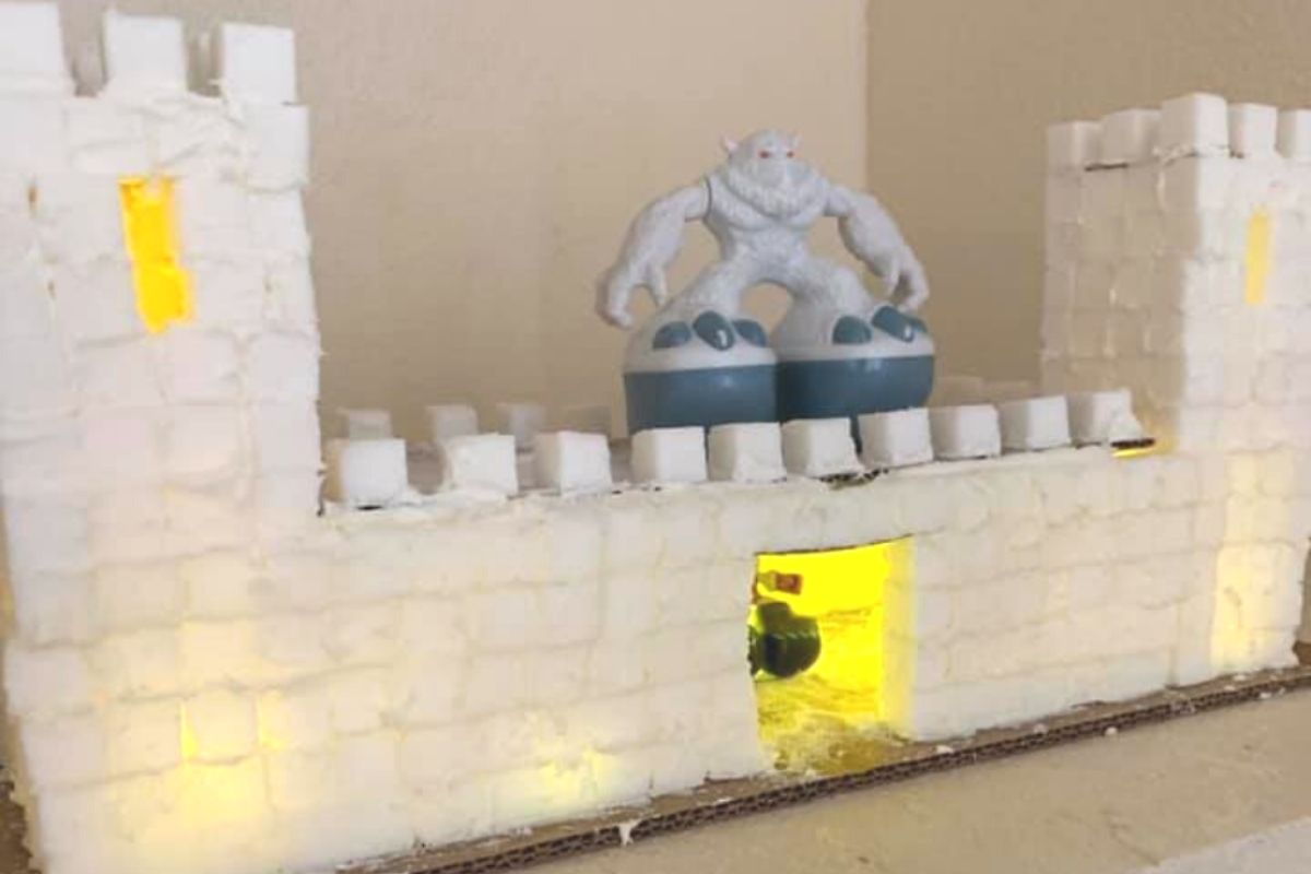 sugar cube castle with two turrets and yeti snowman on top, lit up from inside with battery operated lights