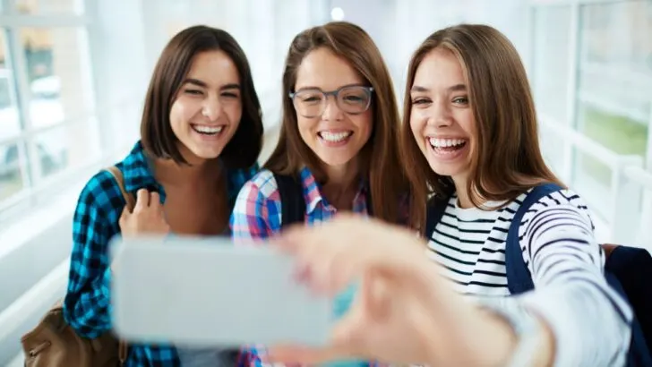 three teen girls taking selfie in school hallway