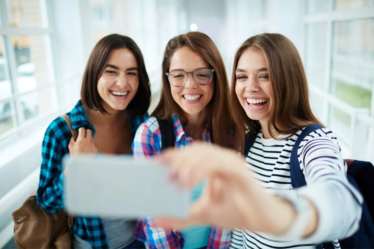 three teen girls taking selfie in school hallway