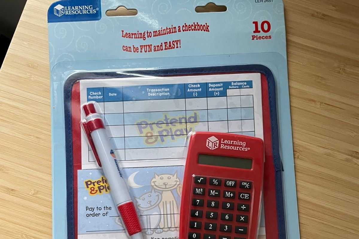 Pretend checks with cats on them, check register, pen, and red calculator package on desk