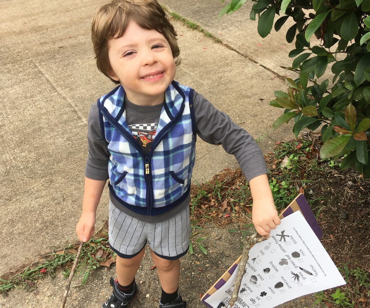 3 year old doing nature scavenger hunt with image printable, smiling, holding sticks