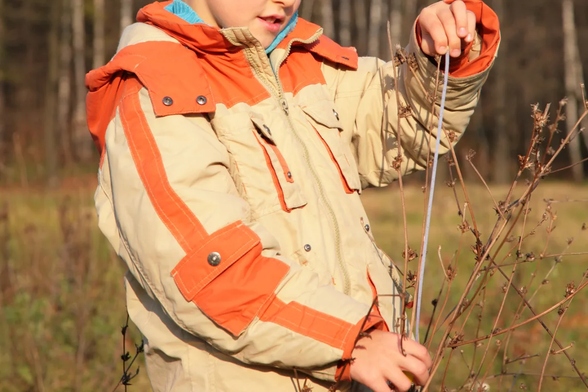 boy holding measuring tape in park along a plant to see how big it is