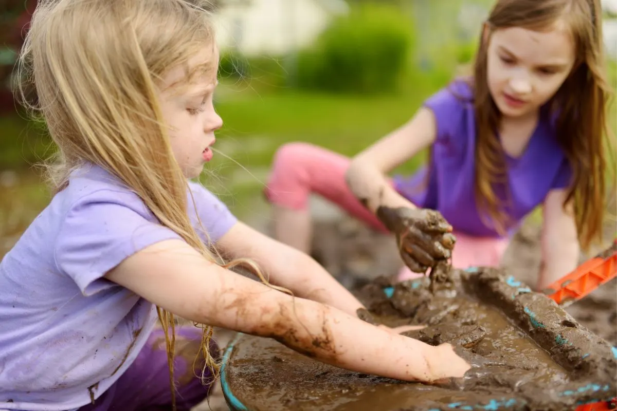 two girls out in backyard playing in mud