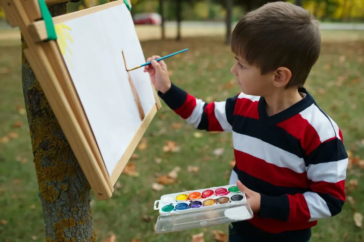 kid painting on canvas taped to a tree