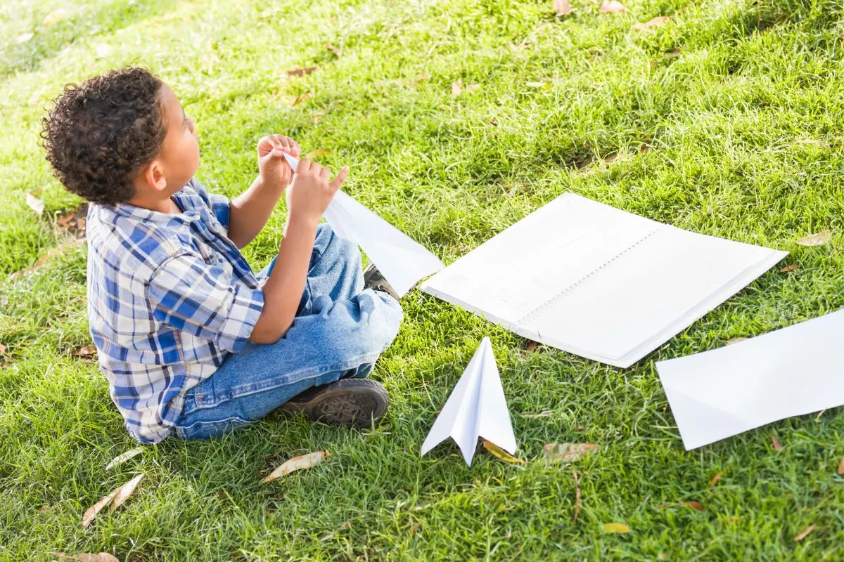 young boy in backyard creating paper airplanes for his paper airplane race