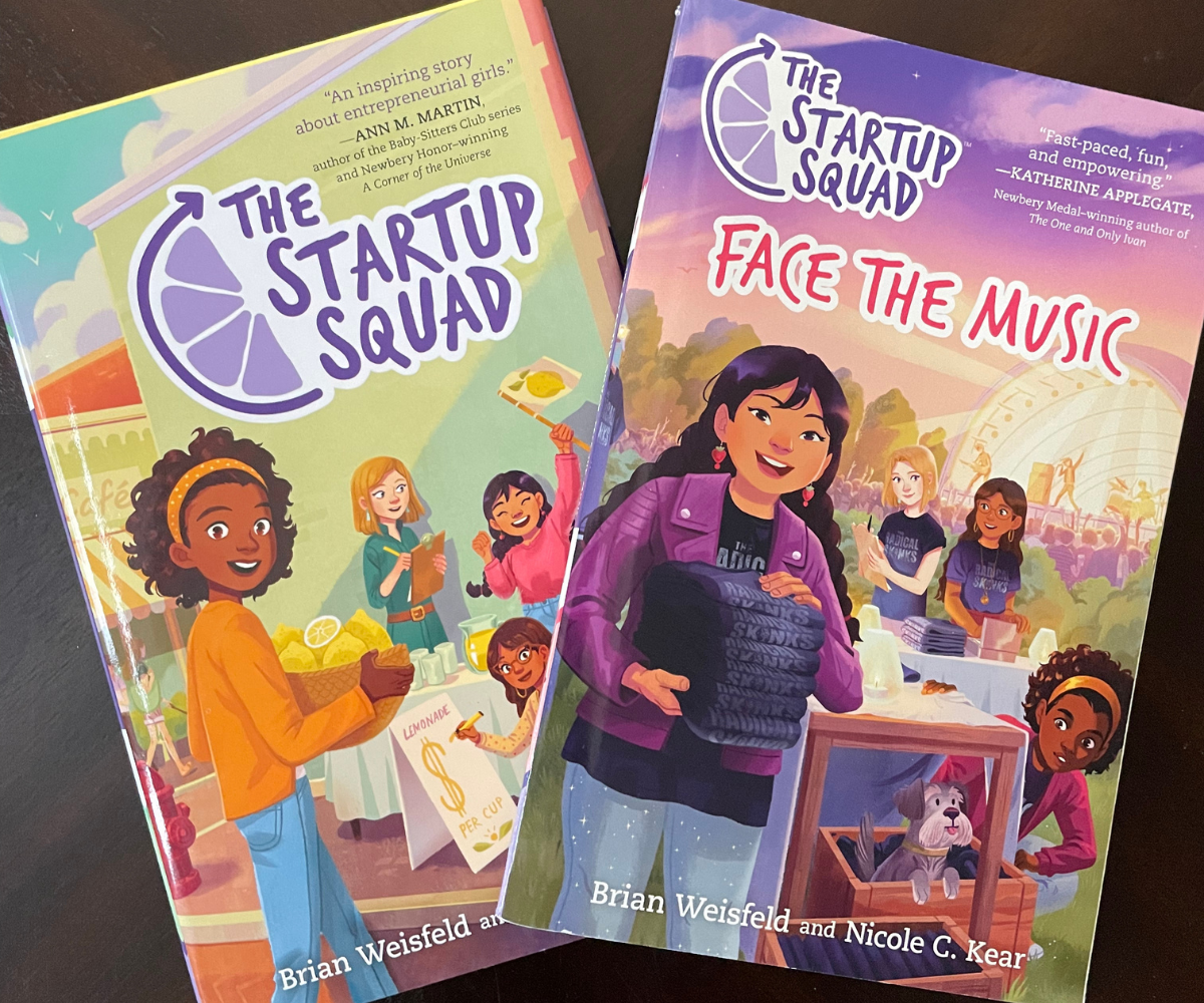 Two teal, purple, and pink colored The Startup Squad books on dark table