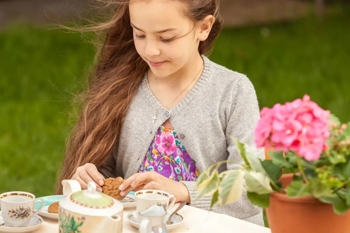 girl with long hair blowing in wind, having afternoon tea and cookies in backyard