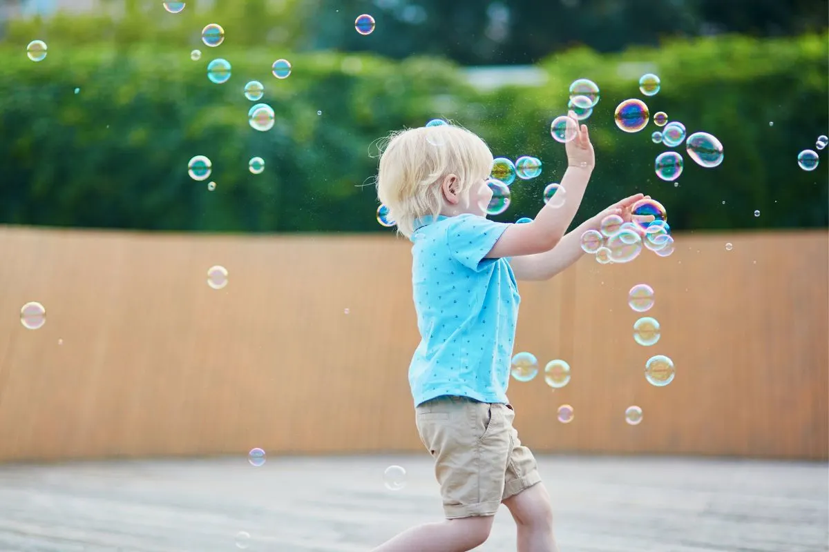 preschooler in bright blue shirt swatting at tons of bubbles having the time of his life outside