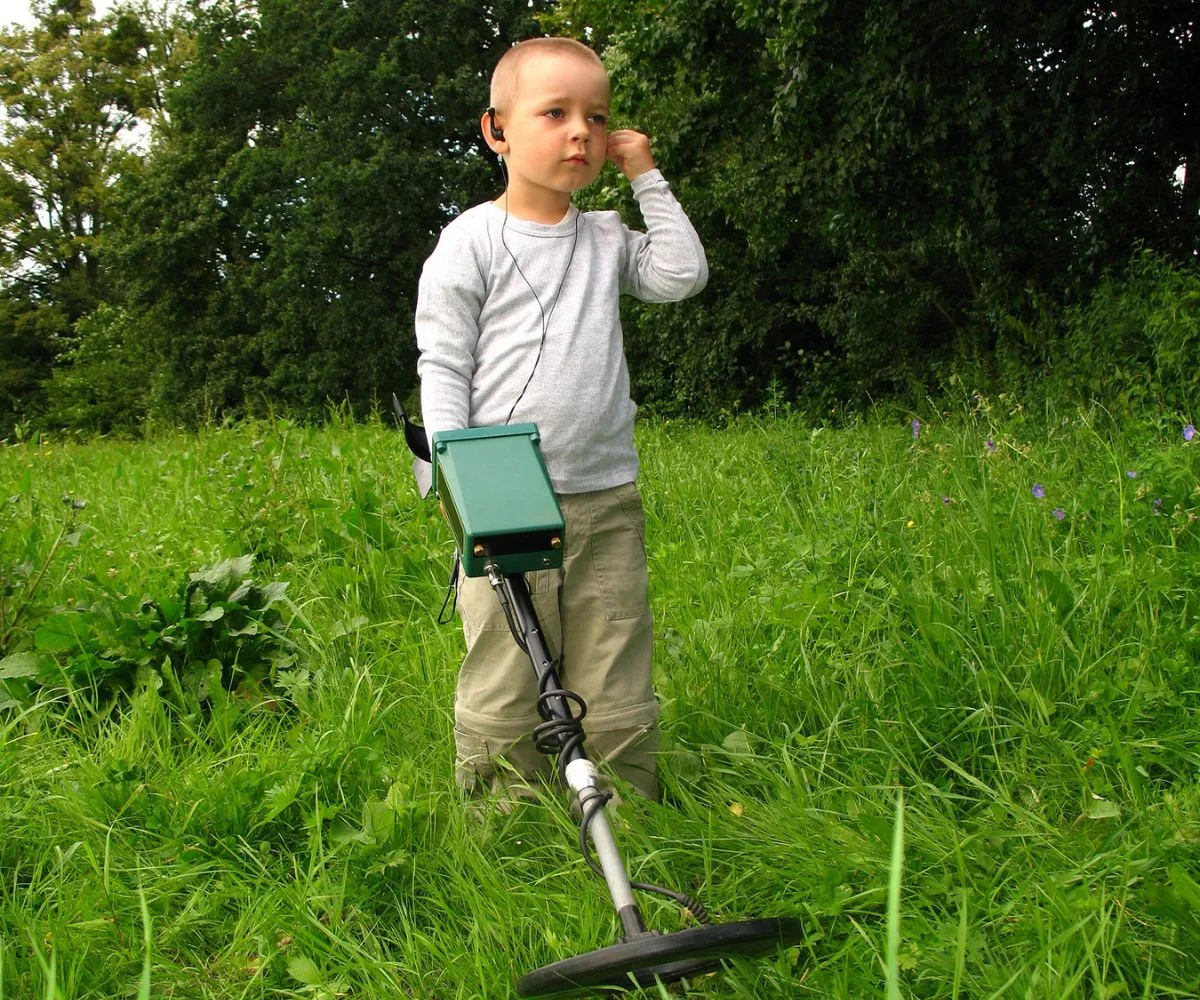 older boy with metal detector, listening, out in backyard field